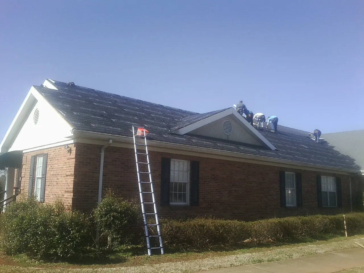 Crew tearing shingles off a brick ranch roof with a ladder set — Metal Roof Repair work by our crew in Clare