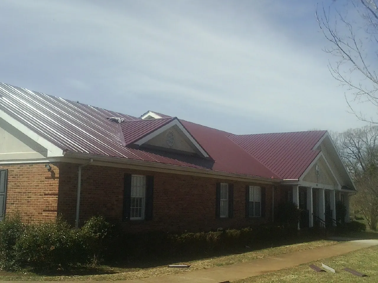 Red metal roof with gabled entries on a long brick building, from a Hail Damage Roof Repair job in Clare